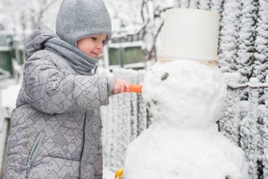 boy makes a snowman. adorable kid boy making a snowman, playing and having fun with snow, outdoors on cold day. active outdoors leisure with children in winter