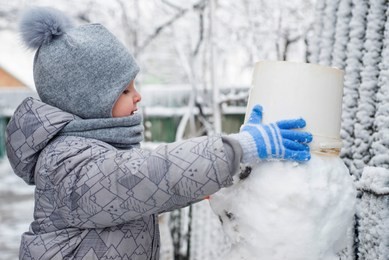 boy makes a snowman. adorable kid boy making a snowman, playing and having fun with snow, outdoors on cold day. active outdoors leisure with children in winter