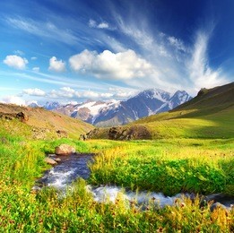 river on bright green meadow. high mountain and clouds.