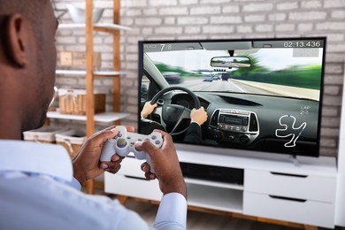 close-up of an african man playing racing game with joystick on television