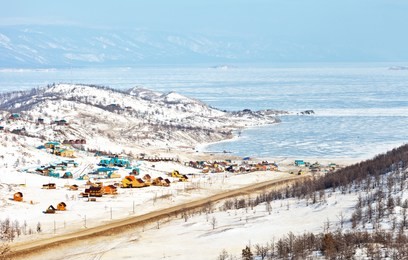 baikal lake in winter. the road to the ice crossing the small sea strait to the olkhon island. tourist wooden houses on the shore of the kurkut bay