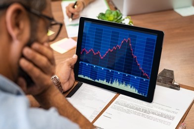 closeup of a stock market broker working with graphs on digital tablet at office. rear view of stock agent reading bad report and graph. back view of multiethnic businessman analyzing fall sales.