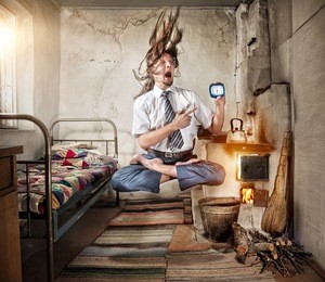 stressful businessman levitating in yoga lotus pose with alarm clock in his hand in old russian house with traditional stove