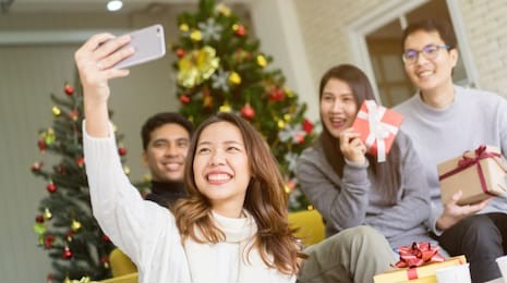 close up group of asian friends using smartphone and take selfie for party group shot in living room with pine tree christmas decoration prepare for celebration festival , relationship cocnept