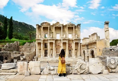 a young asian tourist woman wearing yellow dress enjoying the view at library of celsus at ephesus which is an ancient roman building in ephesus, anatolia and now part of selçuk, turkey.