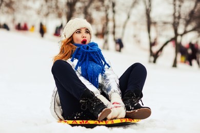 lifestyle portrait of pretty young woman sliding down hill on snow saucer sled outdoors in winter. funny face. emotional photo. winter sports with snow. sledding - fun in the mountains. winter fun 