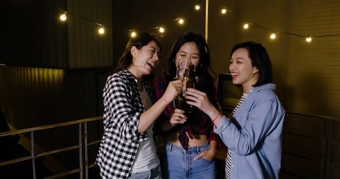 group of girl best friends toasting glasses congratulating. young women clinking champagne together cheerfully celebrating birthday on roof barbecue party at dark night. ladies enjoy having fun.
