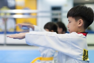 close up short of a young asian boy stretching his arms forward preparing to learn taekwondo - paying respect to taekwondo instructor