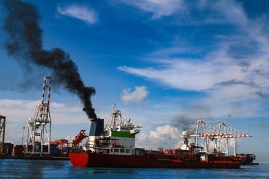 molass red cargo vessel is running out of port. black smoke ejected from the exhaust.