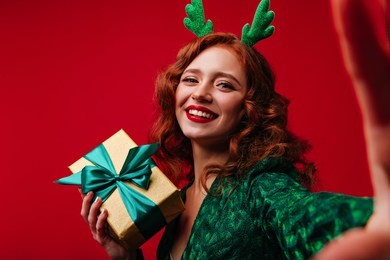 laughing dreamy woman with ginger hair making selfie in christmas. jocund white lady with new year gift smiling to camera.