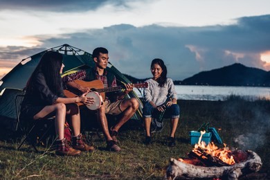 camping tent camp in nature happy friends group night party bonfire and playing guitar together in summer at nature forest