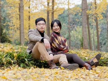 asian couple in love sits on fallen leaves in park. young family and autumn concept. man and woman with smiling faces on autumn trees background. girl and boy or happy lovers on a date.