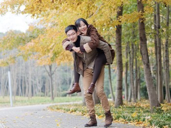 portrait of smiling young girlfriend piggyback boyfriend during romantic walk in autumn park alley, excited couple looking at camera have fun outdoors, playing foolish, man carry lover on his back.