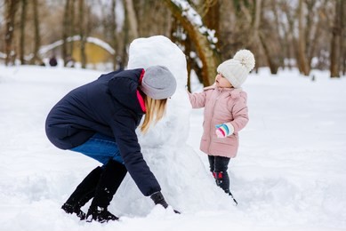 mom and daughter make a snowman out of snow