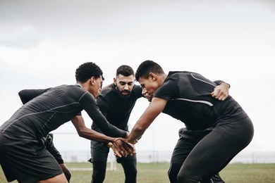 soccer players discussing game strategy standing in a huddle on the ground. footballers standing in a huddle holding hands in the centre.