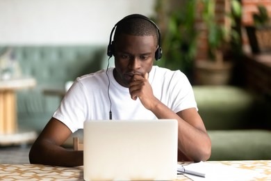focused african american man wear headphones, using laptop, looking at computer screen, thoughtful black student watching video, webinar, learning languages, studying online, making video call
