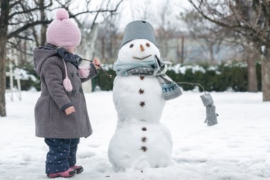 making a snowman and winter fun. cute little girl make a snowman in the winter garden. winter fun activities.