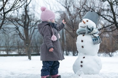 making a snowman and winter fun. cute little girl make a snowman in the winter garden. winter fun activities.