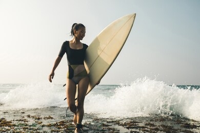 woman surfer with surfboard walking on mossy seashore