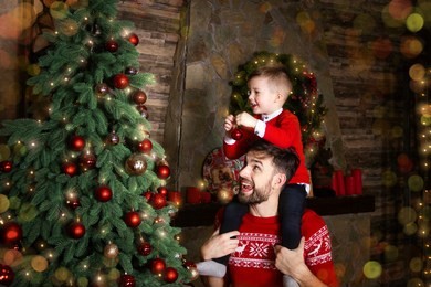 happy father and son enjoying decorating christmas tree with christmas balls and light garland preparing for celebrating winter holidays: merry christmas eve and happy new year 2019. family concept.