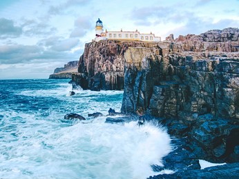 the neist point lighthouse on the end of  world. foamy blue sea strikes against the sharp cliff.  the isle of skye, scotland