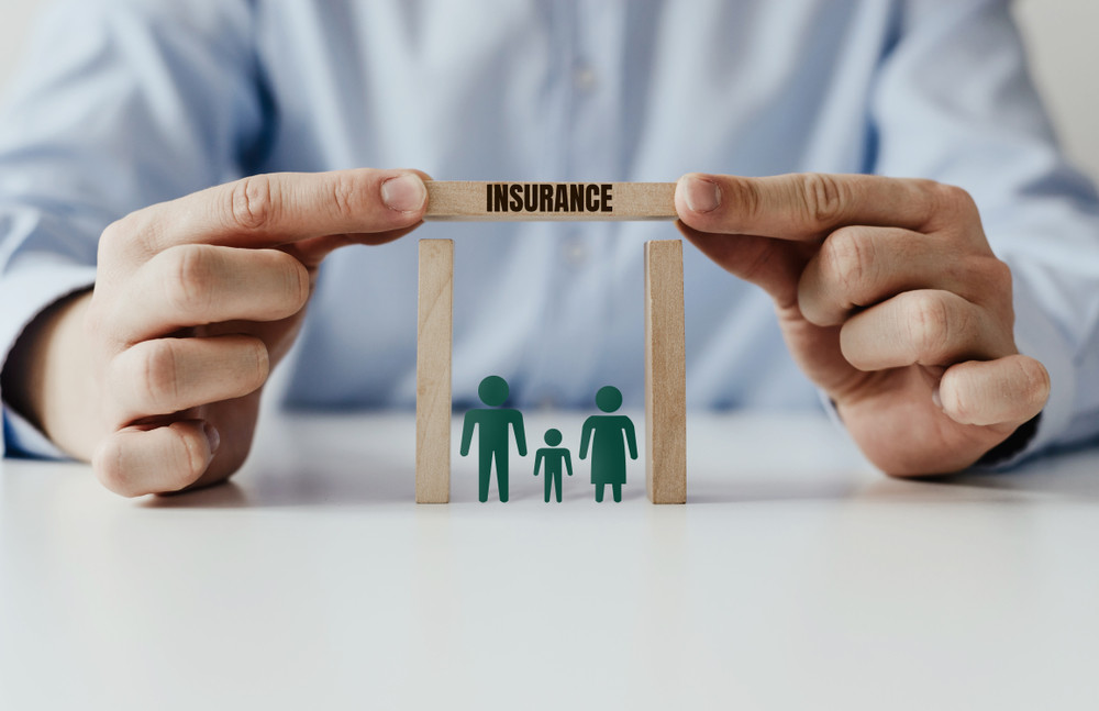 the businessman's hand covers the wooden house with a block with the inscription insurance. family at home with a roof with inscription insurance. family insurance concept.