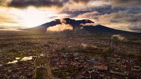 aerial view of bukit tinggi, padang, west sumatra during cloudy hazy morning sunlight. merapi mount and bukit tinggi town as a background