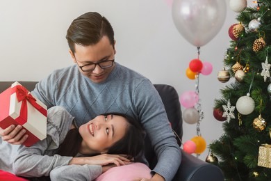 asian men give gift box to beautiful young asian women.smiling face in room with christmas tree decoration for holiday background.lover couple and celebration concept.