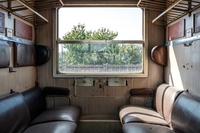 vintage second class cabin in abandoned train  with seats facing each other and sun shining through the open window