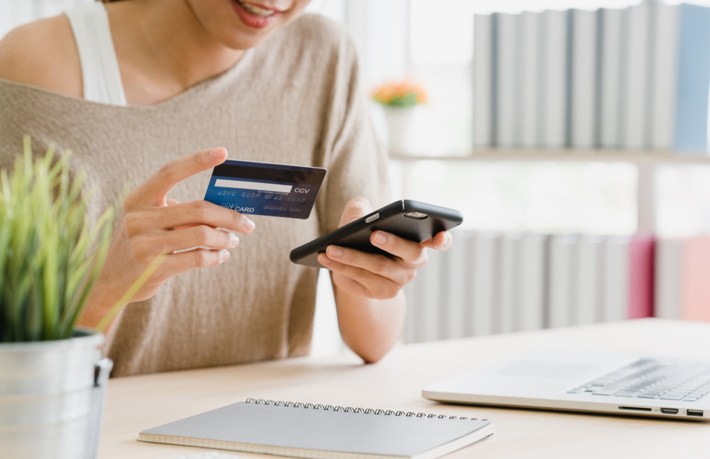 beautiful asian woman using smartphone buying online shopping by credit card while wear sweater sitting on desk in living room at home. lifestyle woman at home concept.
