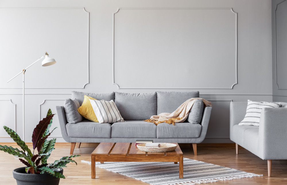 wooden coffee table in the middle of grey living room with couch and copy space on the empty wall, real photo