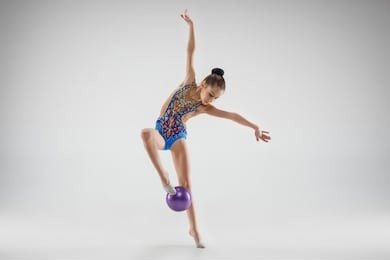 the teen female little girl doing gymnastics exercises with ball on a gray studio background. the gymnastic, stretch, fitness, lifestyle, training, sport concept