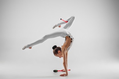 the teen female little girl doing gymnastics exercises with clubs isolated on a gray studio background. the gymnastic, stretch, fitness, lifestyle, training, sport concept