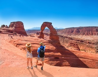 couple on vacation hiking trip. man and woman standing on top of the mountain looking at beautiful view. delicate arch,  moab, utah, arches national park.