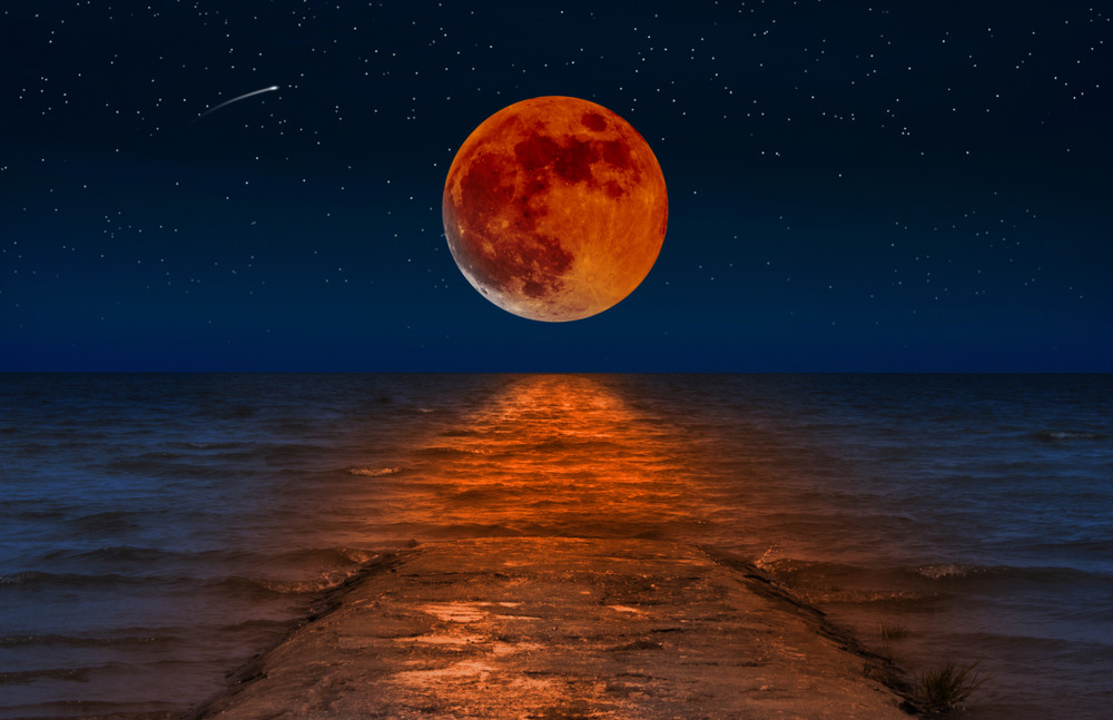 the red full moon is reflected in the starry night in the waves of the sea