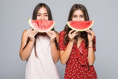 two beautiful young mixed race woman smiling while holding a watermelon in his hands.