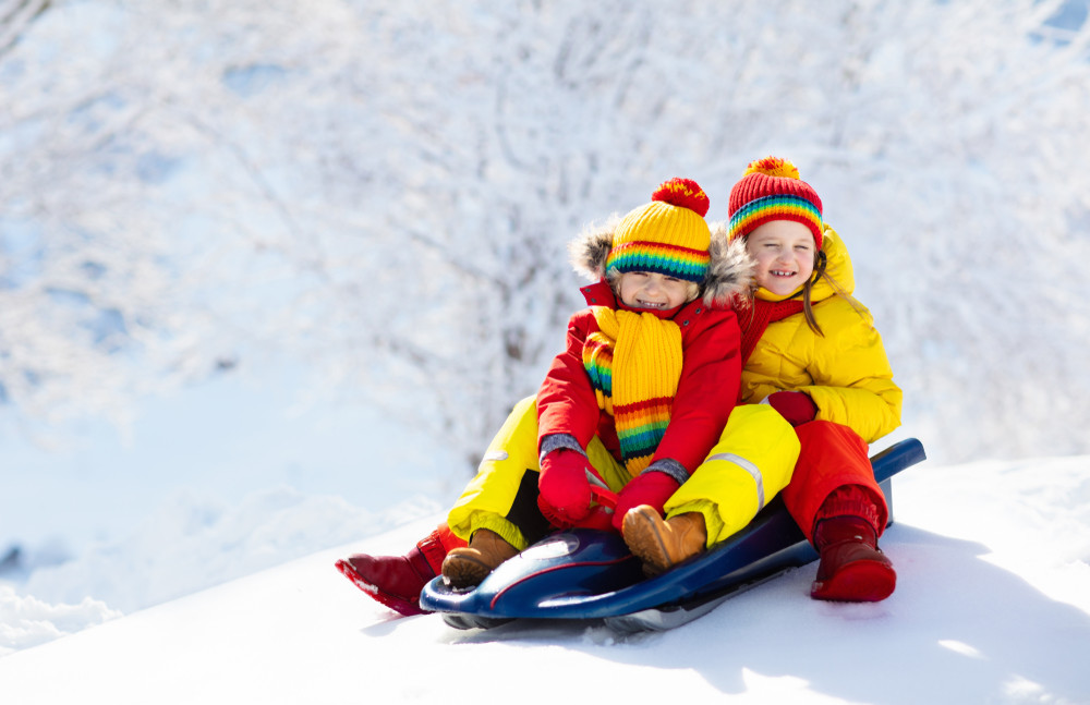 little girl and boy enjoying sleigh ride. child sledding. toddler kid riding a sledge. children play outdoors in snow. kids sled in snowy park in winter. outdoor fun for family christmas vacation.