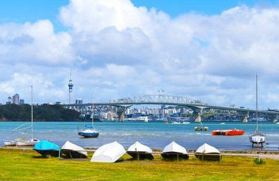 dinghy at little shoal reserve bay beach auckland, new zealand; harbour bridge and auckland city landscape as the background