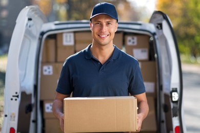 smiling delivery man standing in front of his van