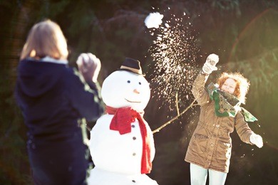 two girls having snowball fight. one of them throwing snowball is in focus, motion blur