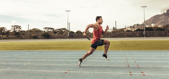 side view of a male athlete sprinting on a running track in a track and field stadium holding a baton. male runner training on a running track.