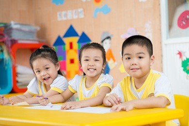three children sitting behind the desk and smiling