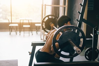 asian man performing barbell squats at the indoor gym.