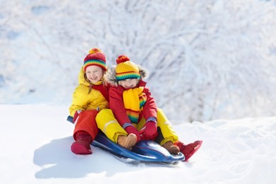 little girl and boy enjoying sleigh ride. child sledding. toddler kid riding a sledge. children play outdoors in snow. kids sled in snowy park in winter. outdoor fun for family christmas vacation.