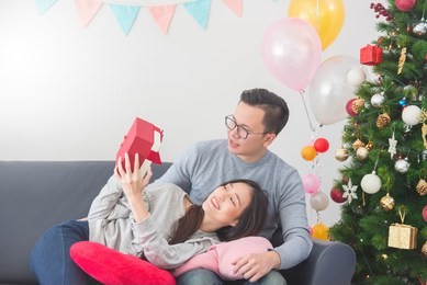 beautiful asian young couple celebrating christmas at home. handsome man giving his girlfriend a gift box.
