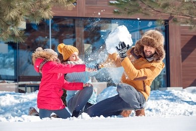 family on a winter vacation spending time together outdoors sitting mother and daughter throwing snow fighting while father holding big snowball up laughing surprised close-up