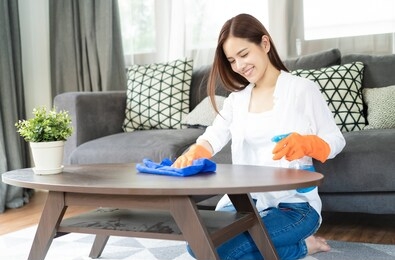 beautiful young asian woman wearing protective gloves cleaning desk by spraying cleaning products and wipes  in living room.