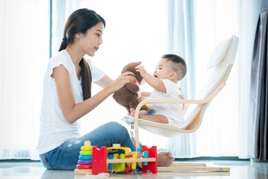asian mother and har baby play teddy bear togather in living room 
