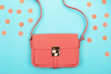 living coral fashion bag and confetti on contrast background. trendy color of 2019 year concept. flat-lay, top view. copy space for your text.