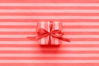 living coral color of the year 2019 gift box with bow on striped wrapping paper. abstract geometric background.
